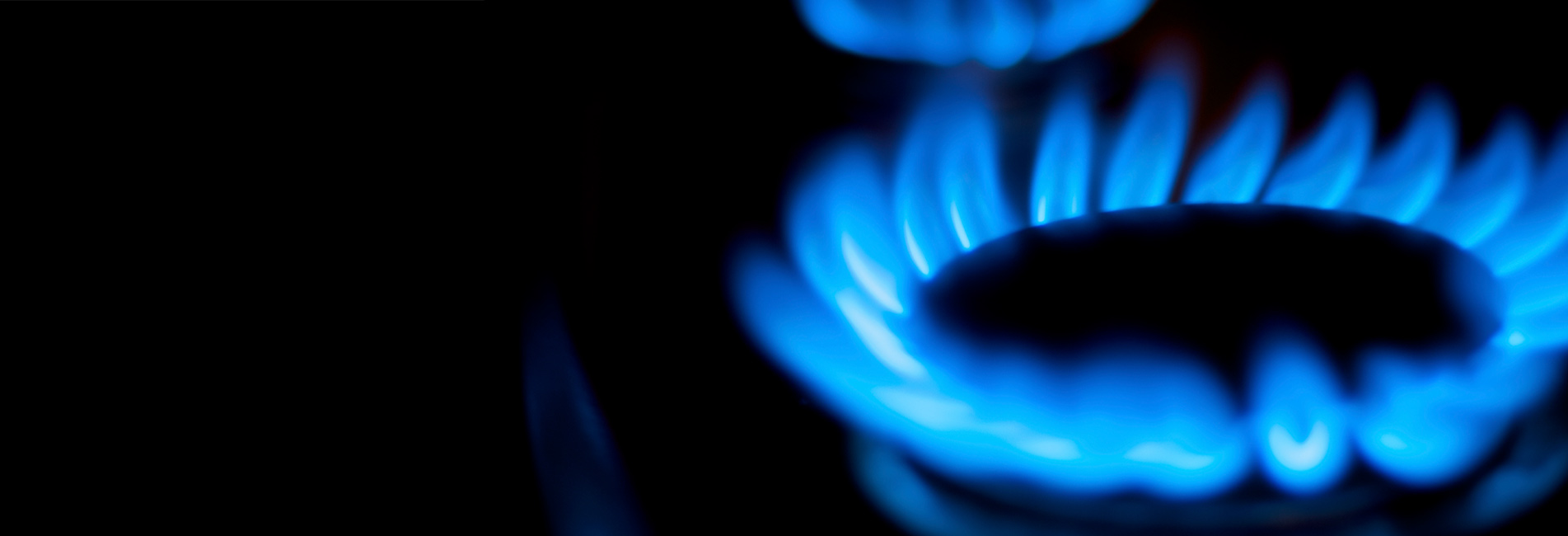 The image displays a close-up of a gas burner flame, characterised by vibrant blue flames that appear to flicker and dance. The flame is surrounded by a dark backdrop, highlighting the brightness and intensity of the gas flame, which is typically used in cooking or heating.