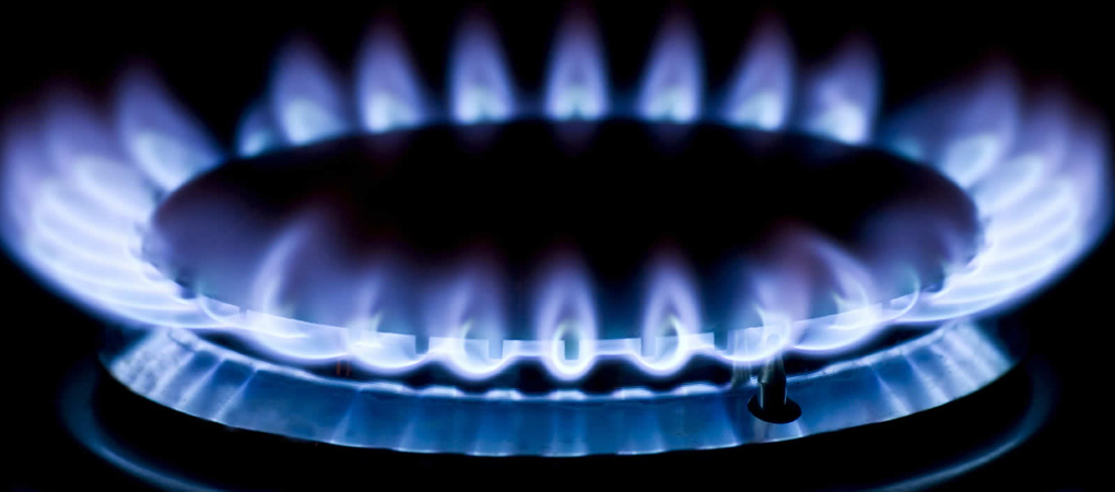 The image features a gas stove burner with vibrant blue flames emanating from a circular metal burner. The flames appear steady and evenly distributed, set against a dark background, highlighting the intensity and energy of the gas flames.